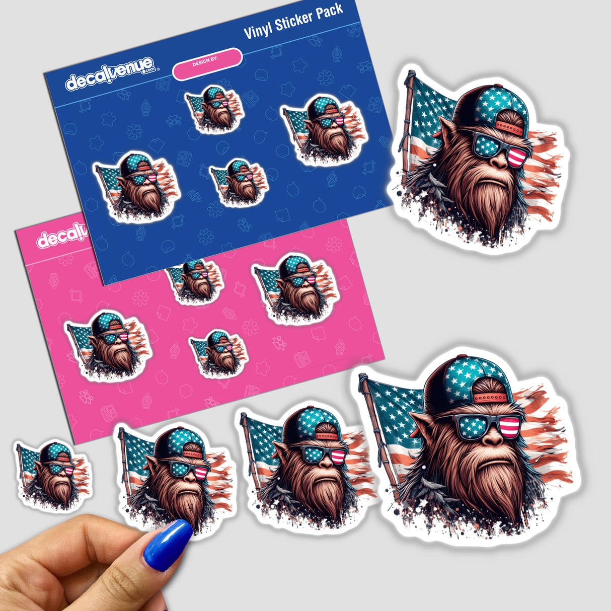 Sticker pack featuring a Vintage American Flag Sasquatch design, held in a hand with blue nail polish, includes cartoon illustrations of a monkey in sunglasses and a bearded man wearing sunglasses.