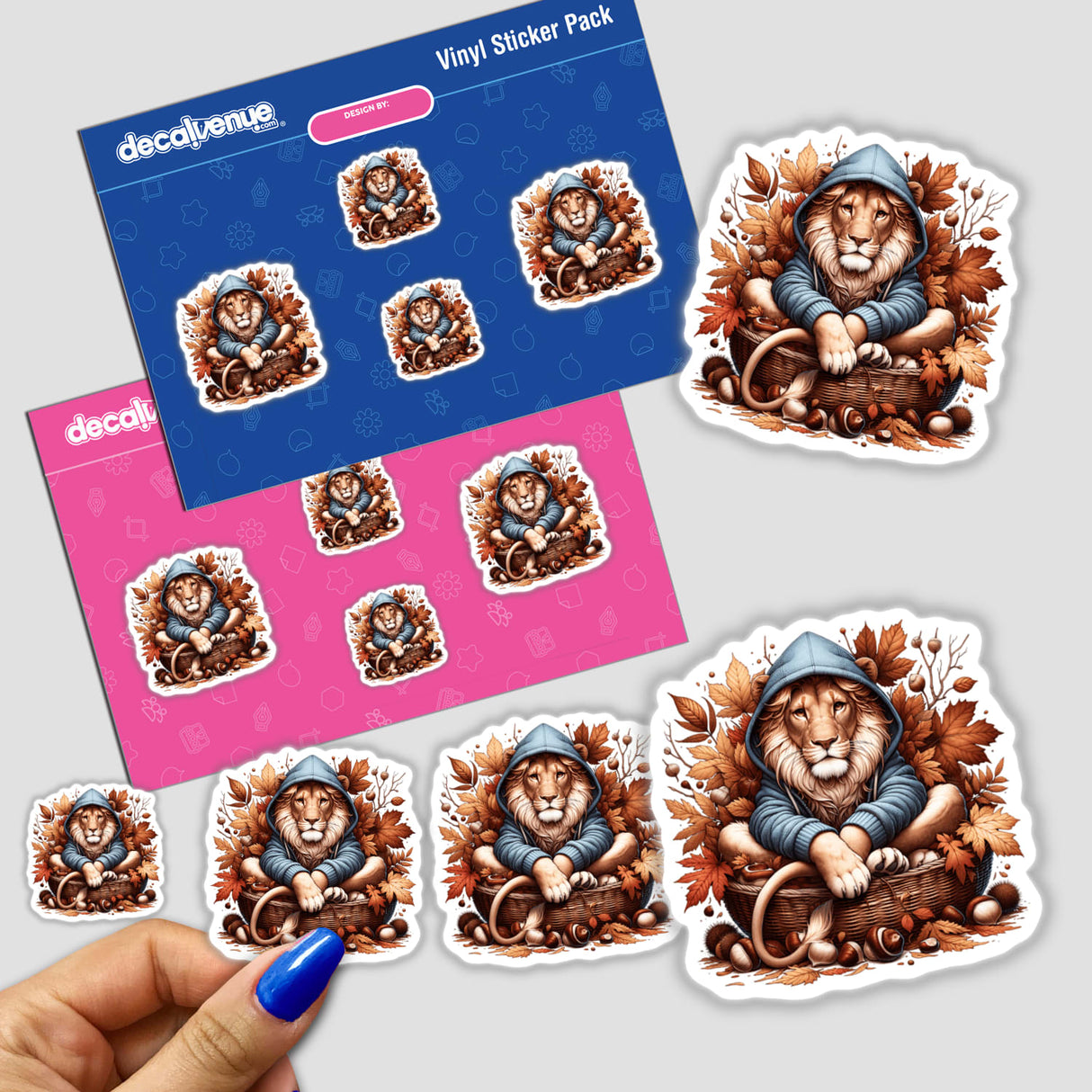 Autumn Lion in Cozy Sweater sticker featuring a cartoon lion nestled in a basket with leaves and acorns. Available as stickers or digital artwork from Decal Venue.