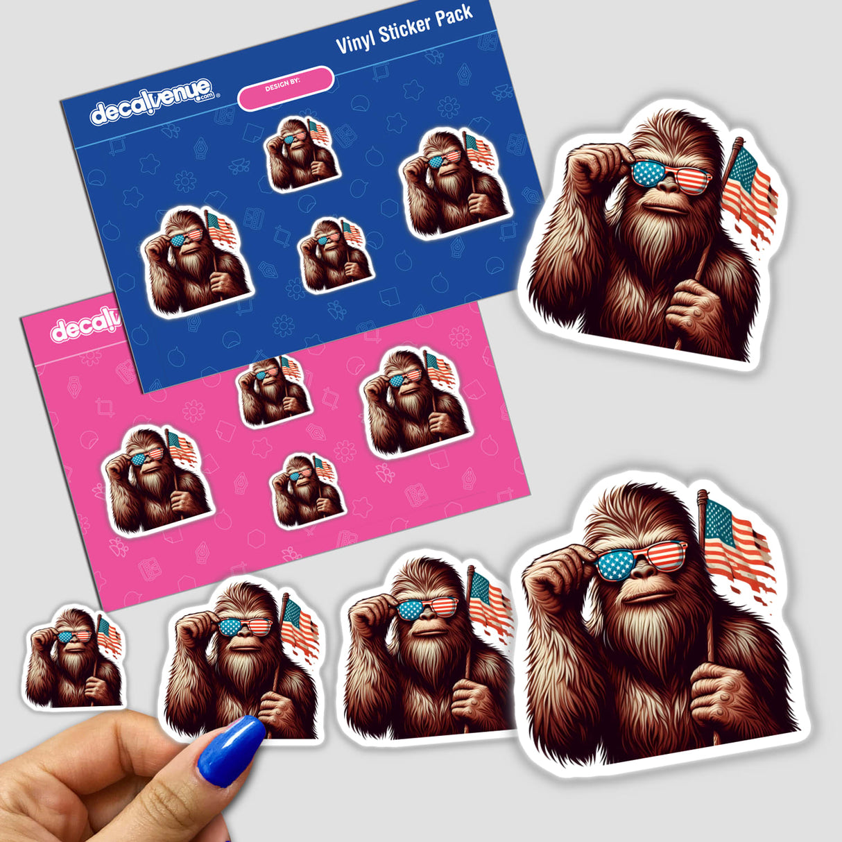 Sasquatch Holding American Flag vinyl sticker pack from Decal Venue, featuring die-cut stickers with Bigfoot tipping star-spangled sunglasses, available on two backing sheets. Hand shown peeling a larger sticker.
