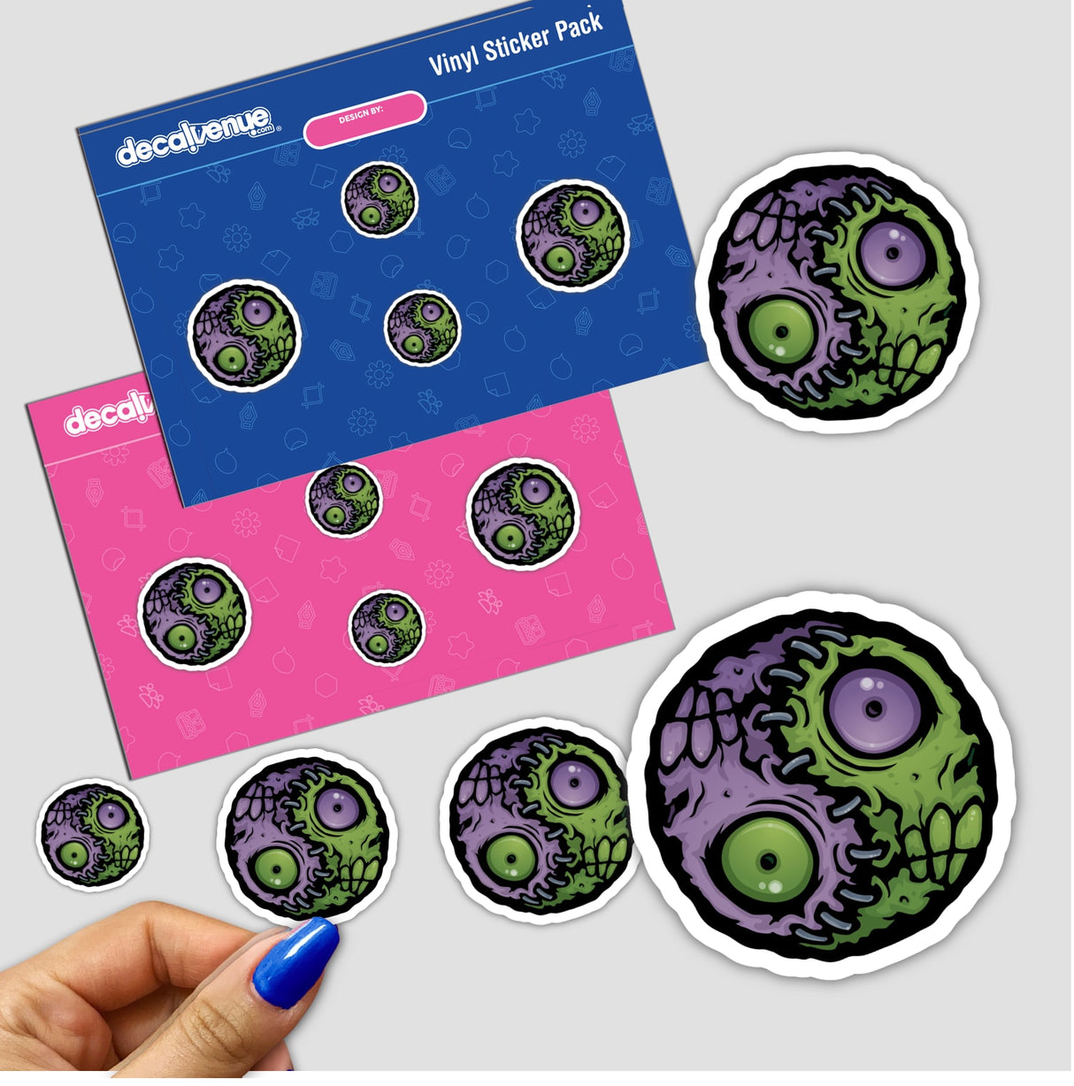Zombie Yin-Yang sticker featuring a cartoon zombie and skull, held in a hand with blue nail polish. Available individually or in a sticker pack.