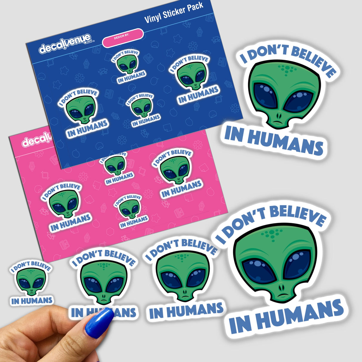I Don’t Believe In Humans Cartoon Alien sticker featuring a green alien face with blue eyes, held by a hand with blue nail polish. Available as stickers or digital artwork.