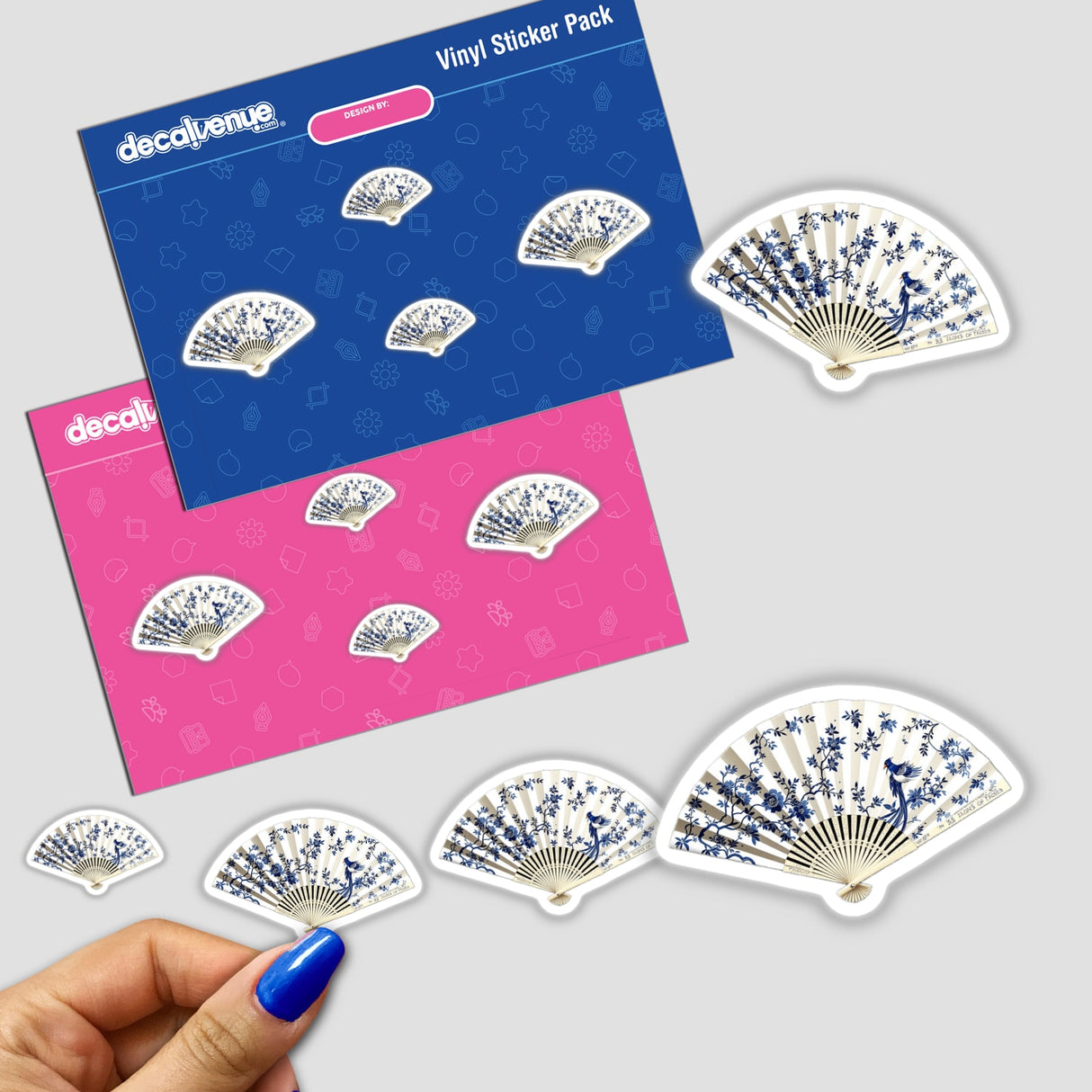 Hand holds a Chinoiserie Fan sticker from Decal Venue, showcasing intricate blue and pink designs, part of a sticker pack. Available as stickers or digital artwork.